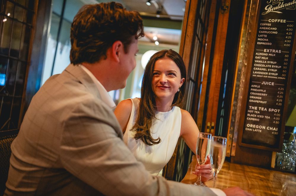 Two people having an animated conversation at a cozy bar or restaurant with warm lighting and wooden decor.