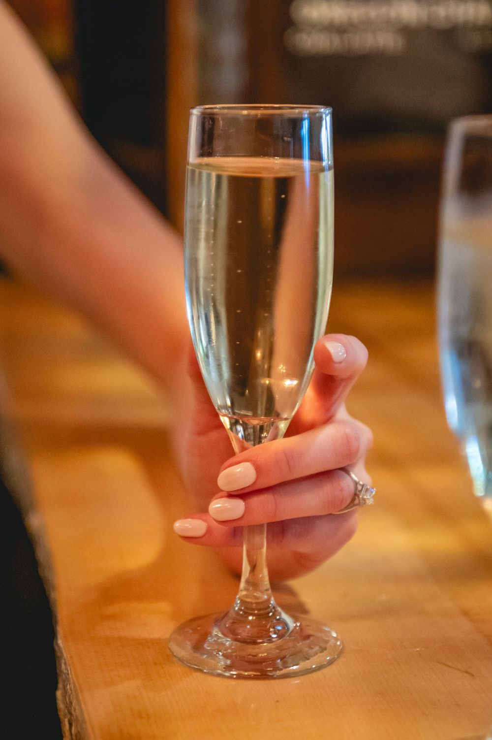 A hand holding a small glass of clear liquid on a wooden bar counter with multiple similar glasses in sequence.
