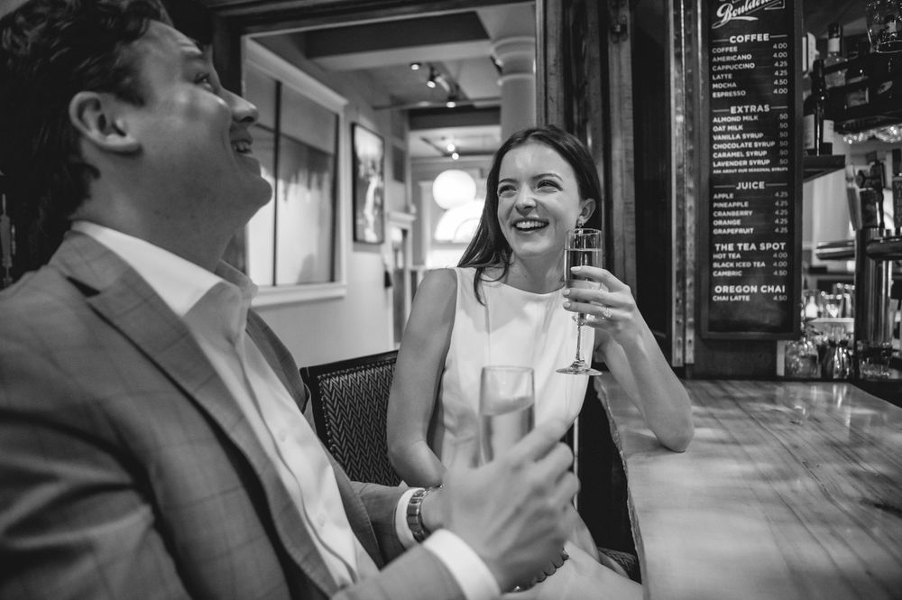 People sharing drinks and laughter at a rustic bar counter with wine glasses.