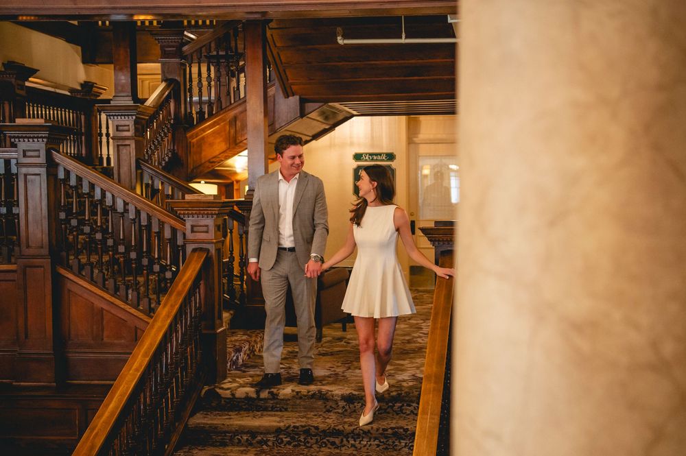 Bride and groom walk up elegant wooden staircase in romantic lighting at their wedding venue.