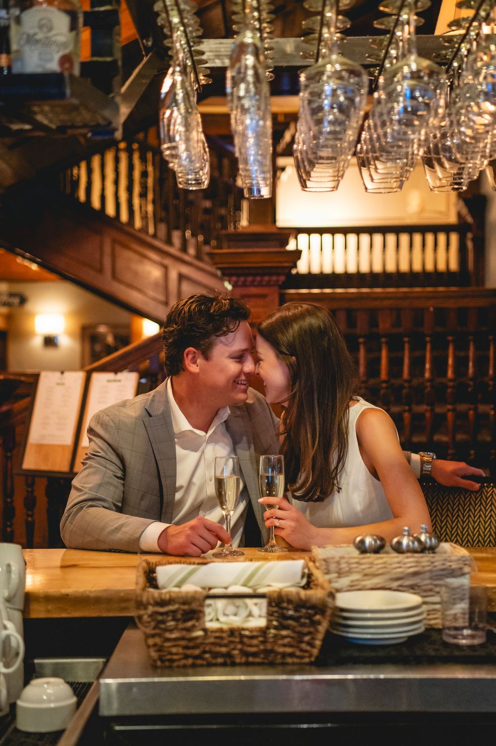 A romantic couple shares an intimate moment at a restaurant bar under warm lighting and hanging glass pendant lamps.