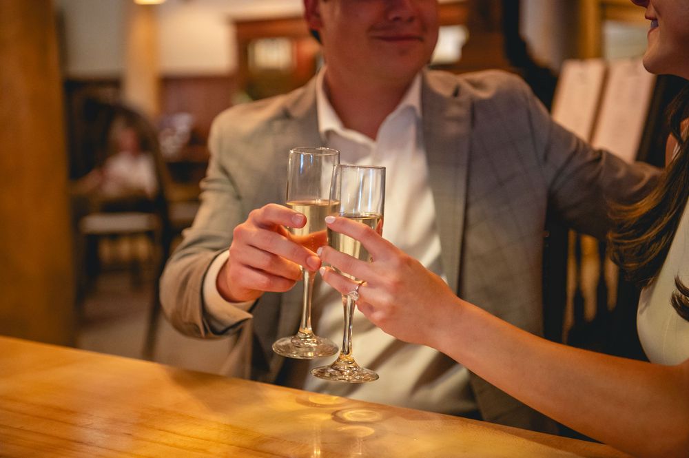 Two people toasting with champagne glasses at a restaurant table in warm lighting.