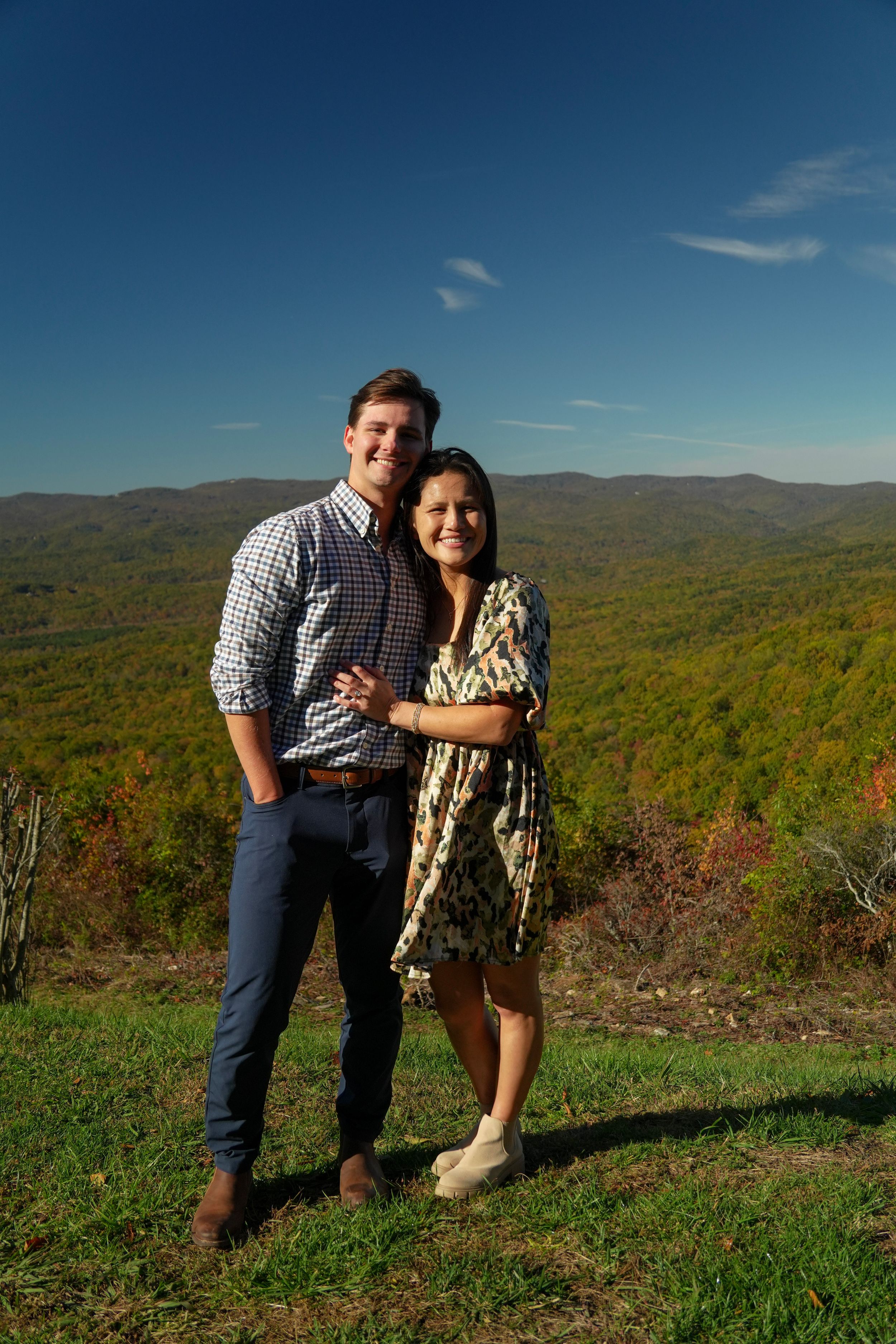 Smiling couple embracing on a hilltop with vibrant fall mountain landscape in the background.