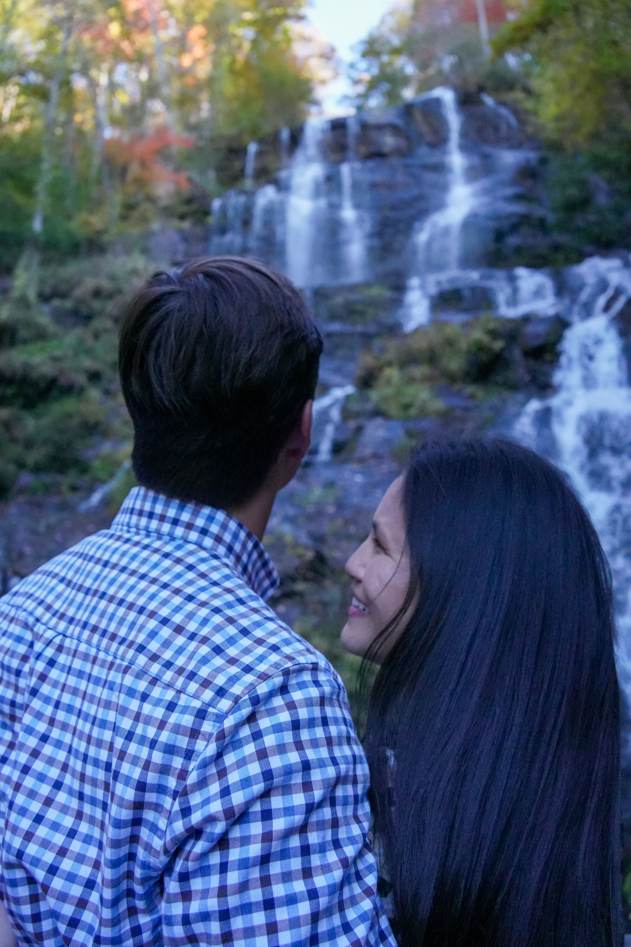 Couple gazing at a cascading waterfall surrounded by colorful autumn foliage in a serene forest setting.
