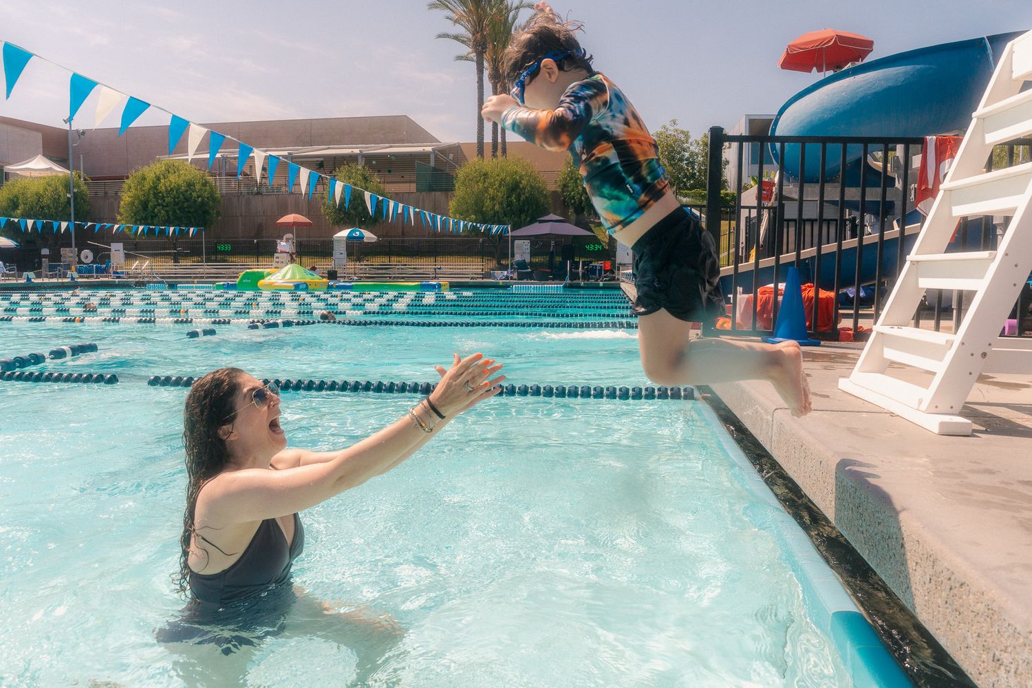 Toddler's expression of joy during first time jumping into blue pool and being caught by mom in the water - Mariano Alvarez photography.