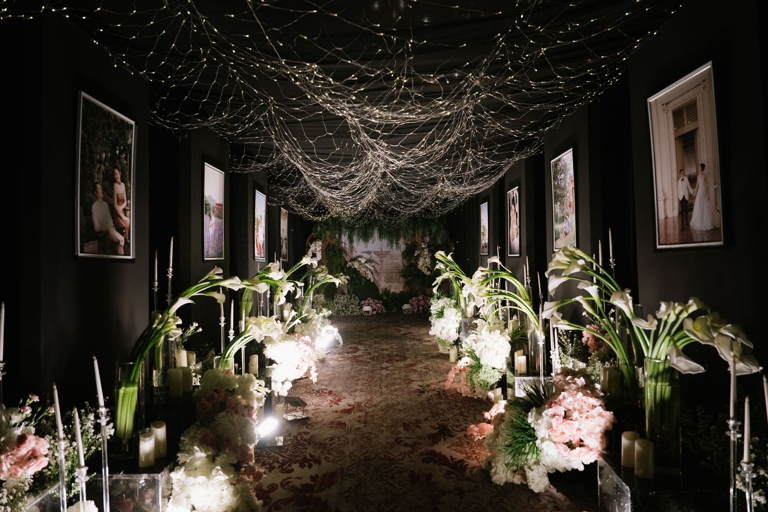 Romantic dark wedding aisle decorated with fairy lights ceiling installation, candles, and lush floral arrangements.