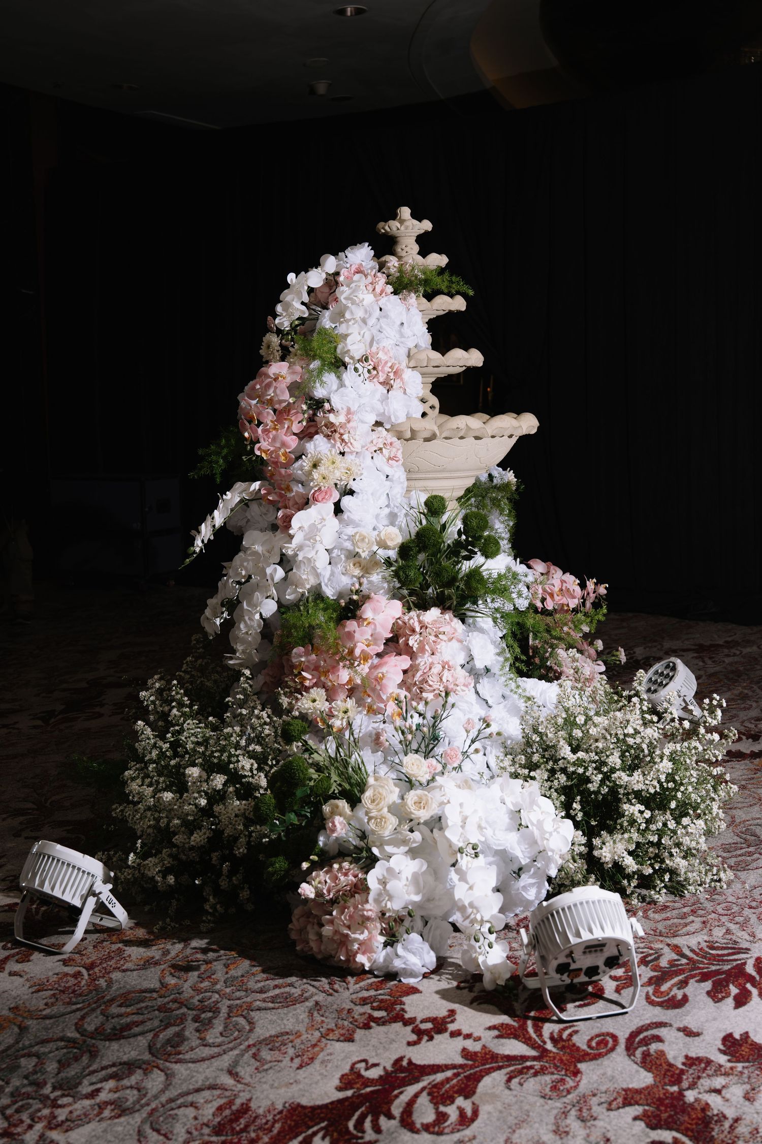 Elaborate white and pink floral arrangement surrounding a decorative fountain centerpiece at a wedding reception.