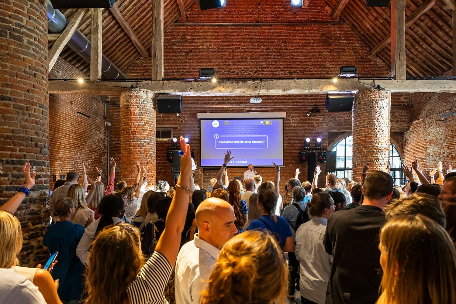Audience in a brick-walled venue watching a presentation on a large screen.