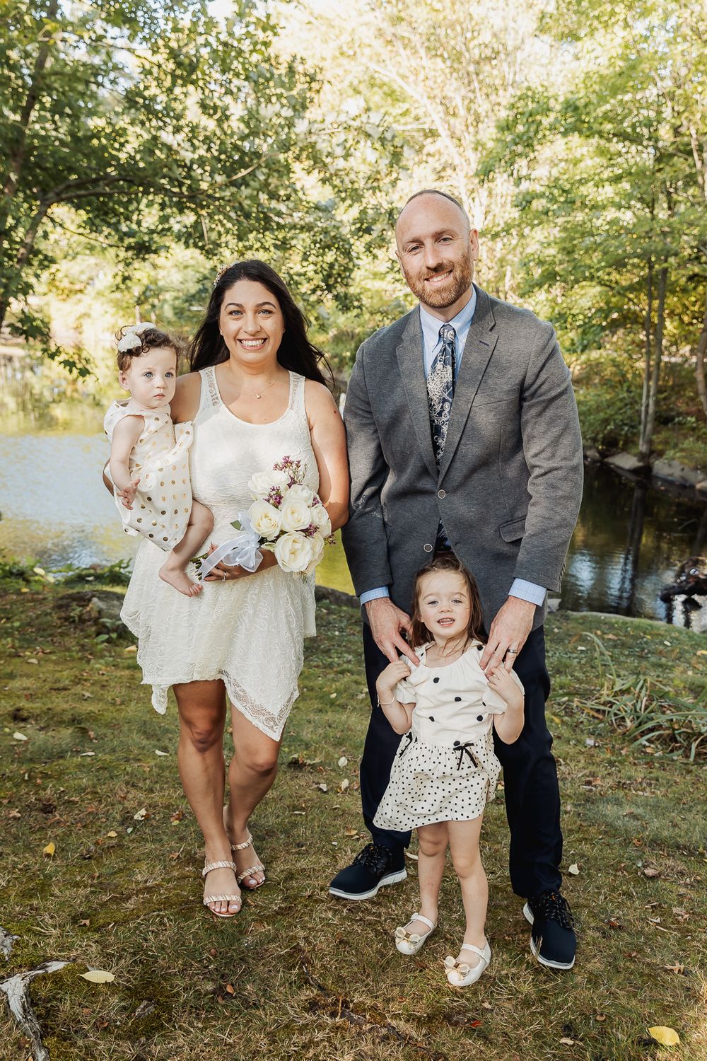 A family enjoys a casual outdoor photoshoot together by a lake on a sunny autumn day.