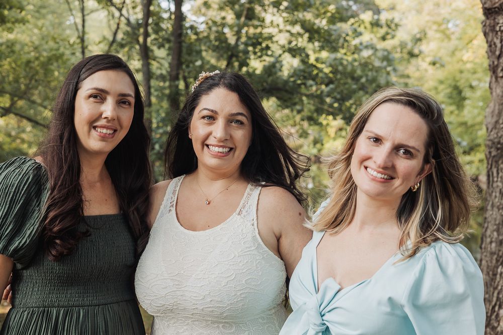 A group of friends smiling together outdoors with green trees and natural lighting in the background.