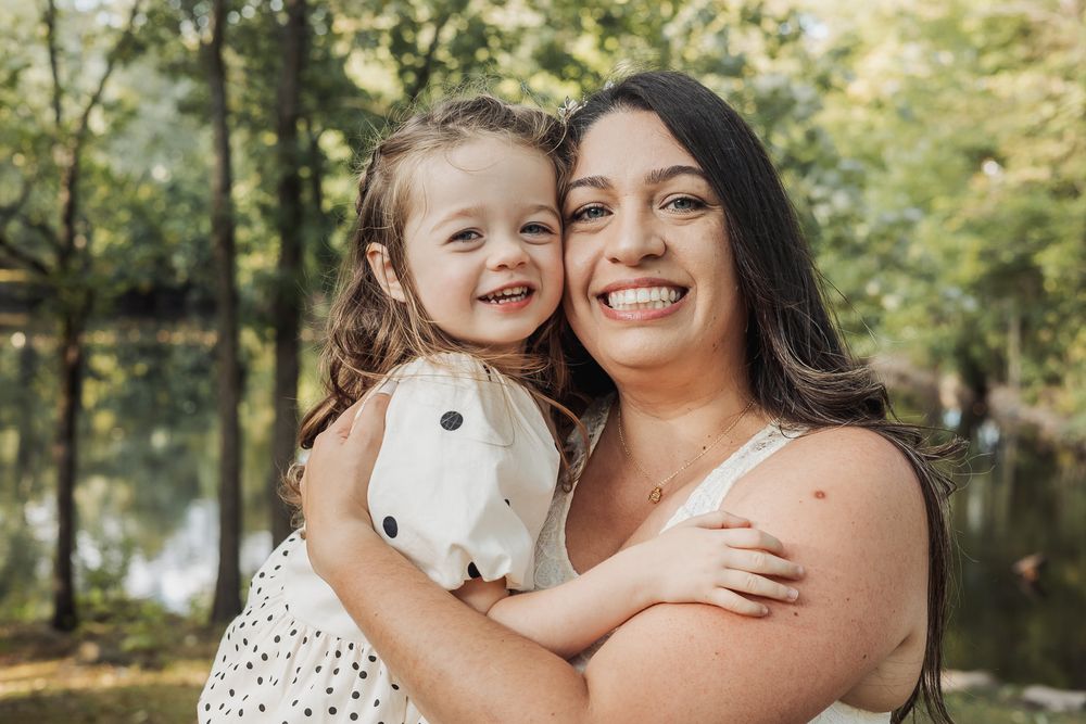 A happy outdoor portrait in nature with a white polka dot dress and long dark hair against a green forest background.