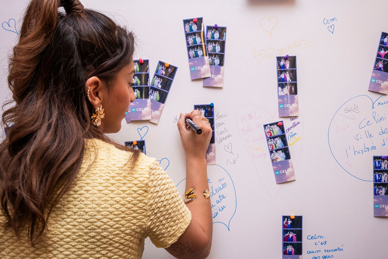 Person examining photos and notes posted on a white wall in an office setting.