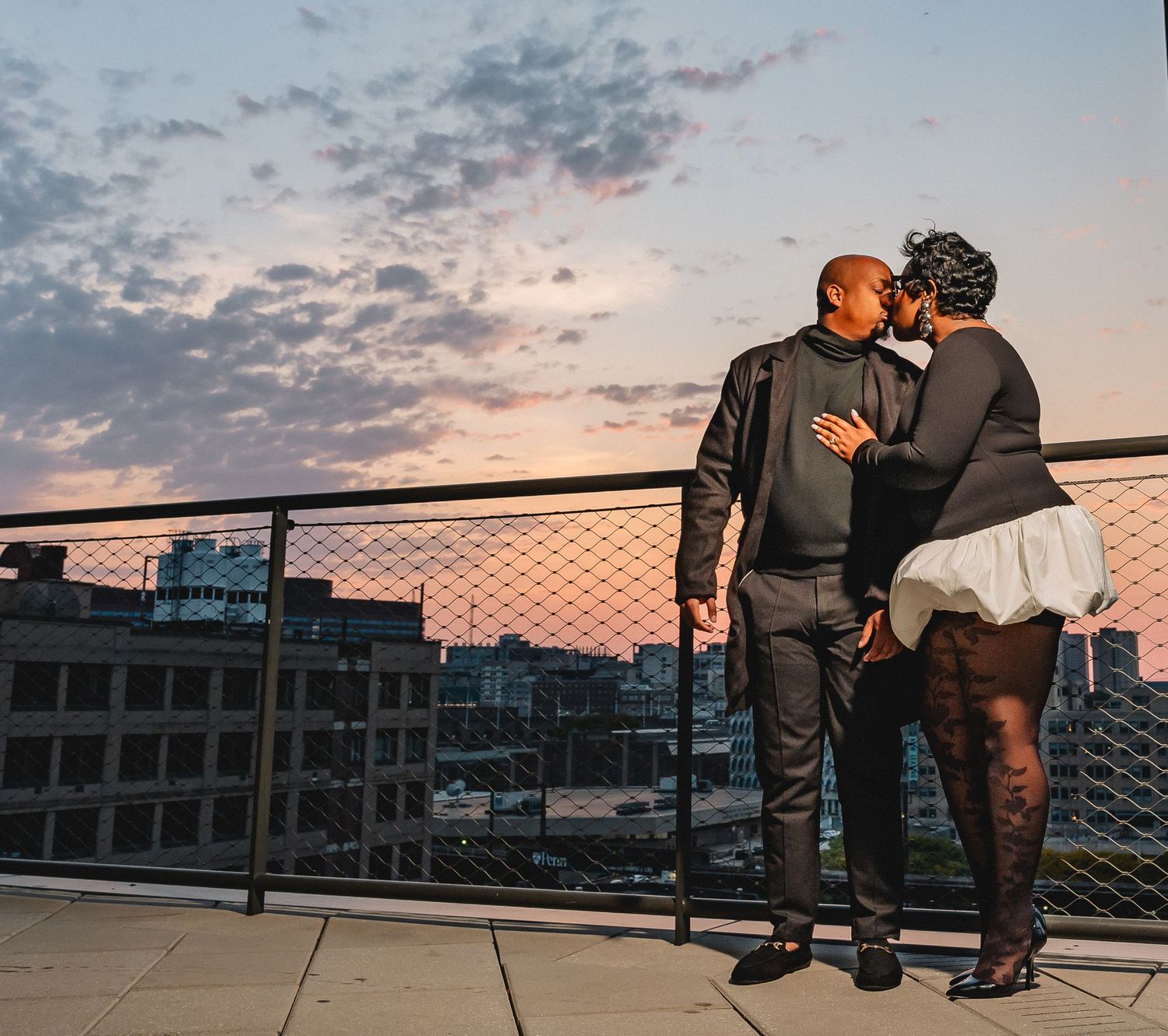 A couple dances together on a path next to a stone church building with a glass conservatory in the background.