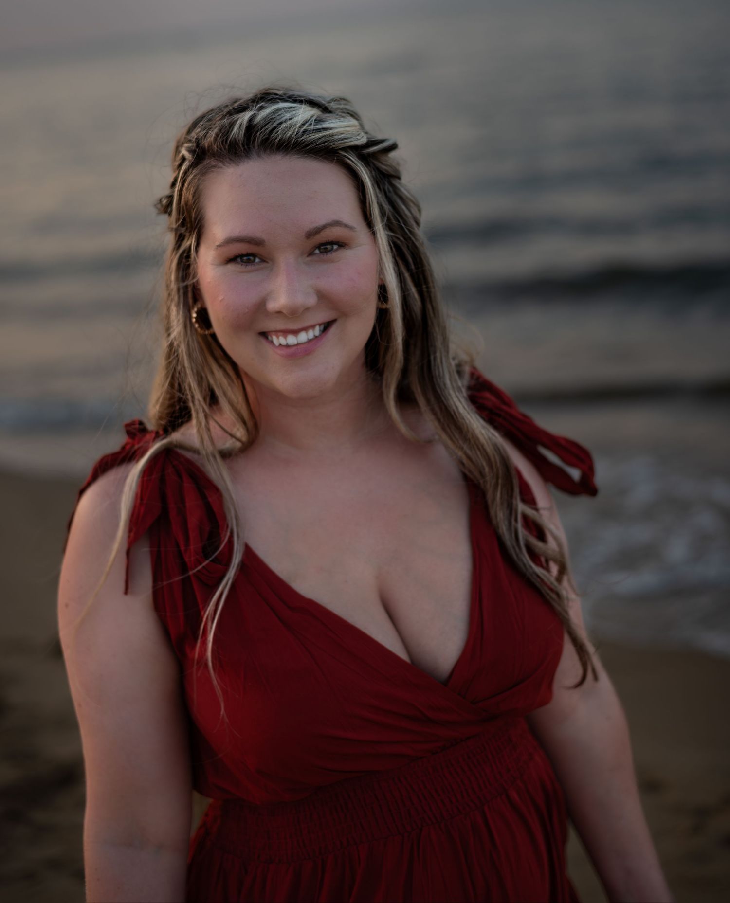 Boudoir photography of a portrait on the beach of a woman with a red dress smiling at the camera
