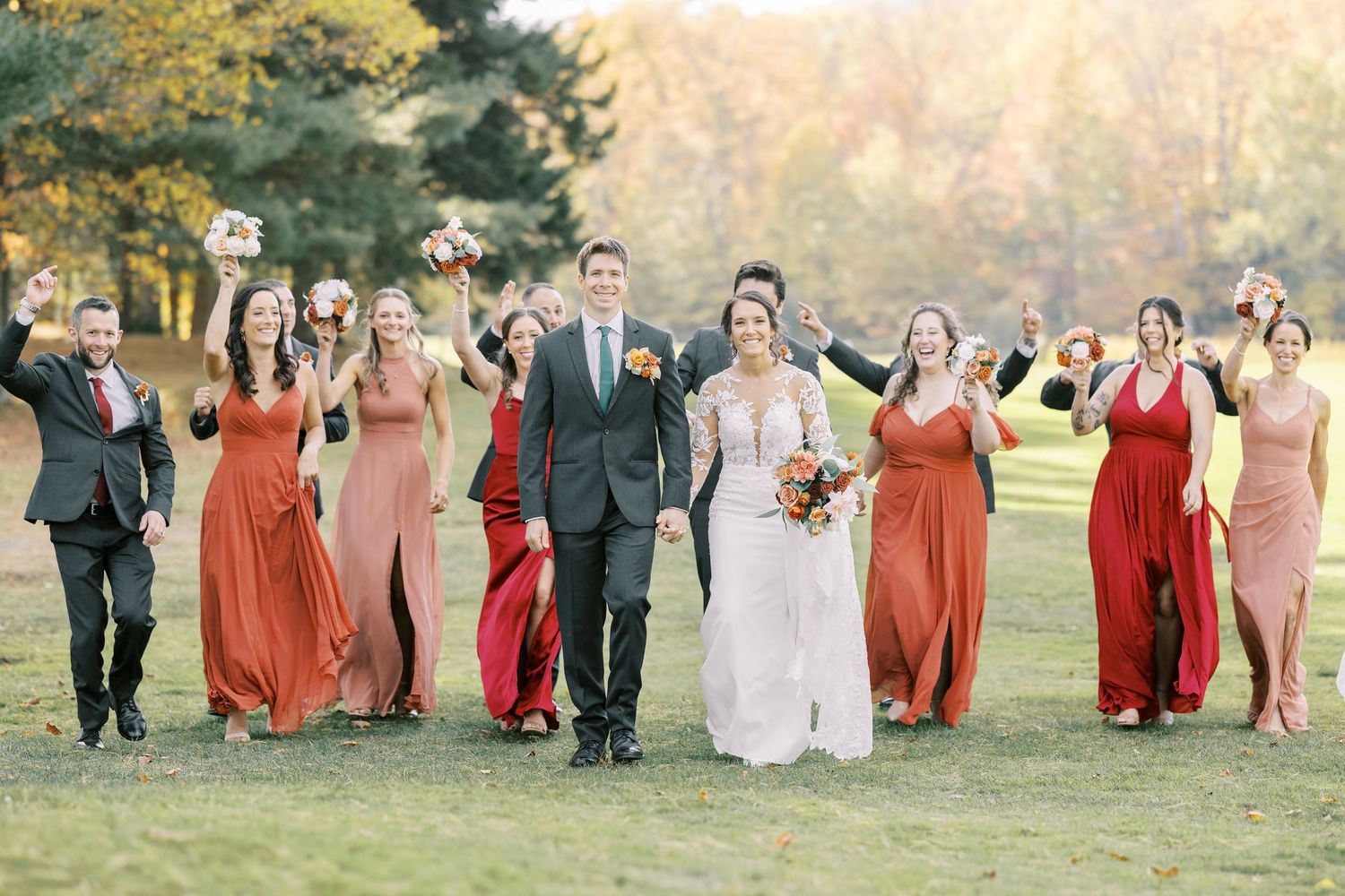 Wedding party in red and pink dresses walking together on a grassy lawn during golden hour.
