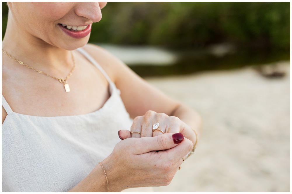 Close up of hands holding a sparkling engagement ring on a beach.