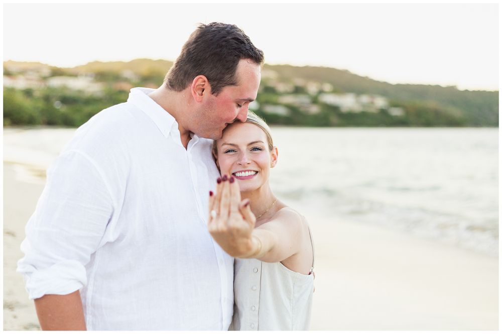 A romantic couple embraces on a beach at sunset wearing white clothing.