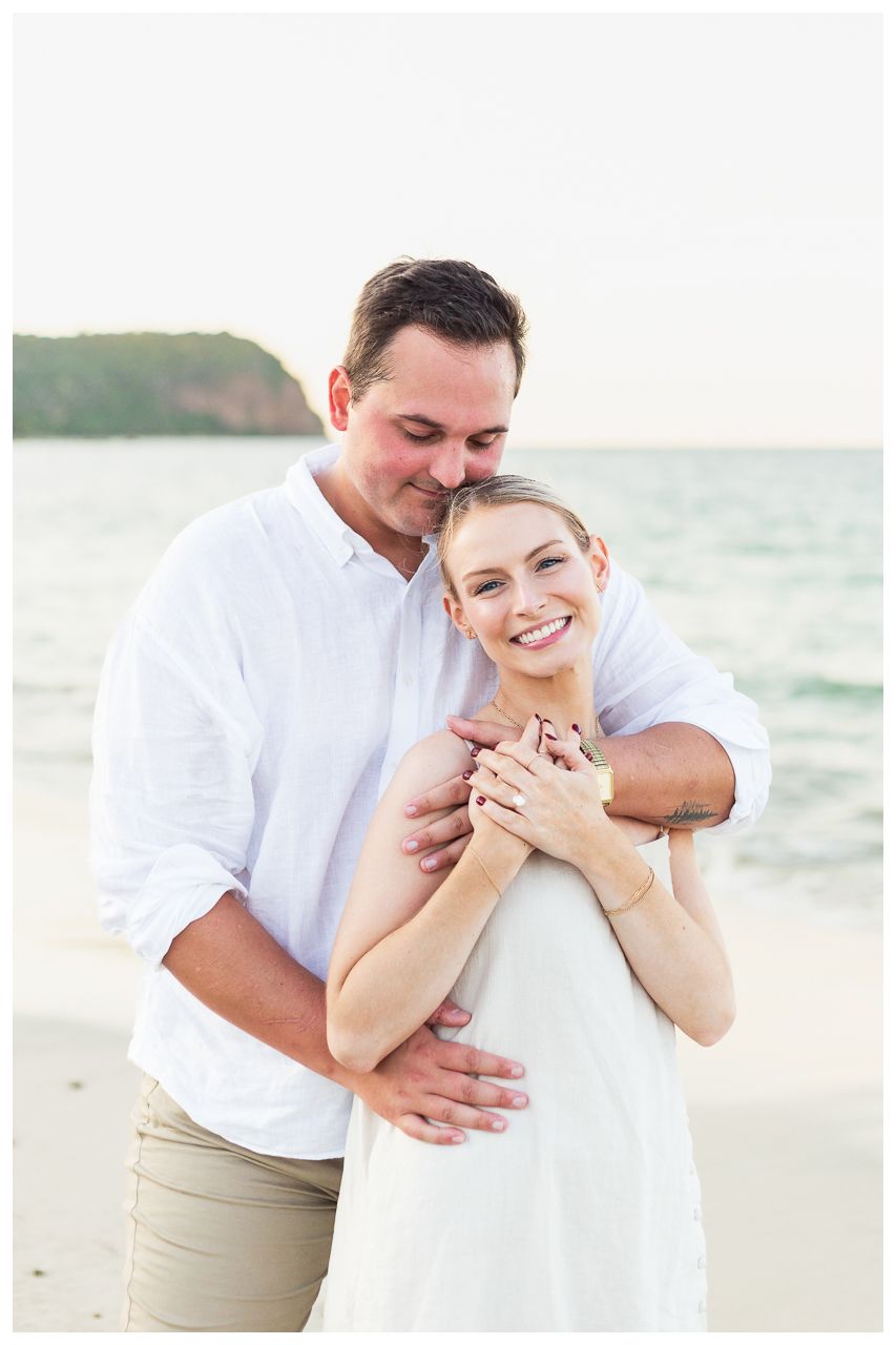 A couple shares a romantic moment together on a beach with ocean waves in the background.