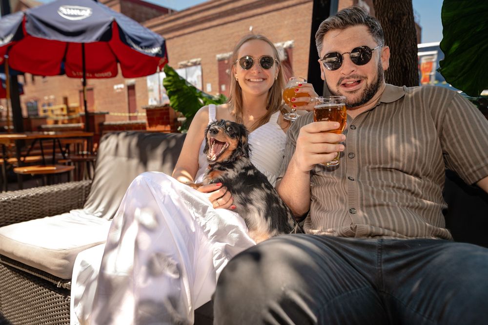 A group of people enjoying drinks and conversation at an outdoor restaurant patio on a sunny day.