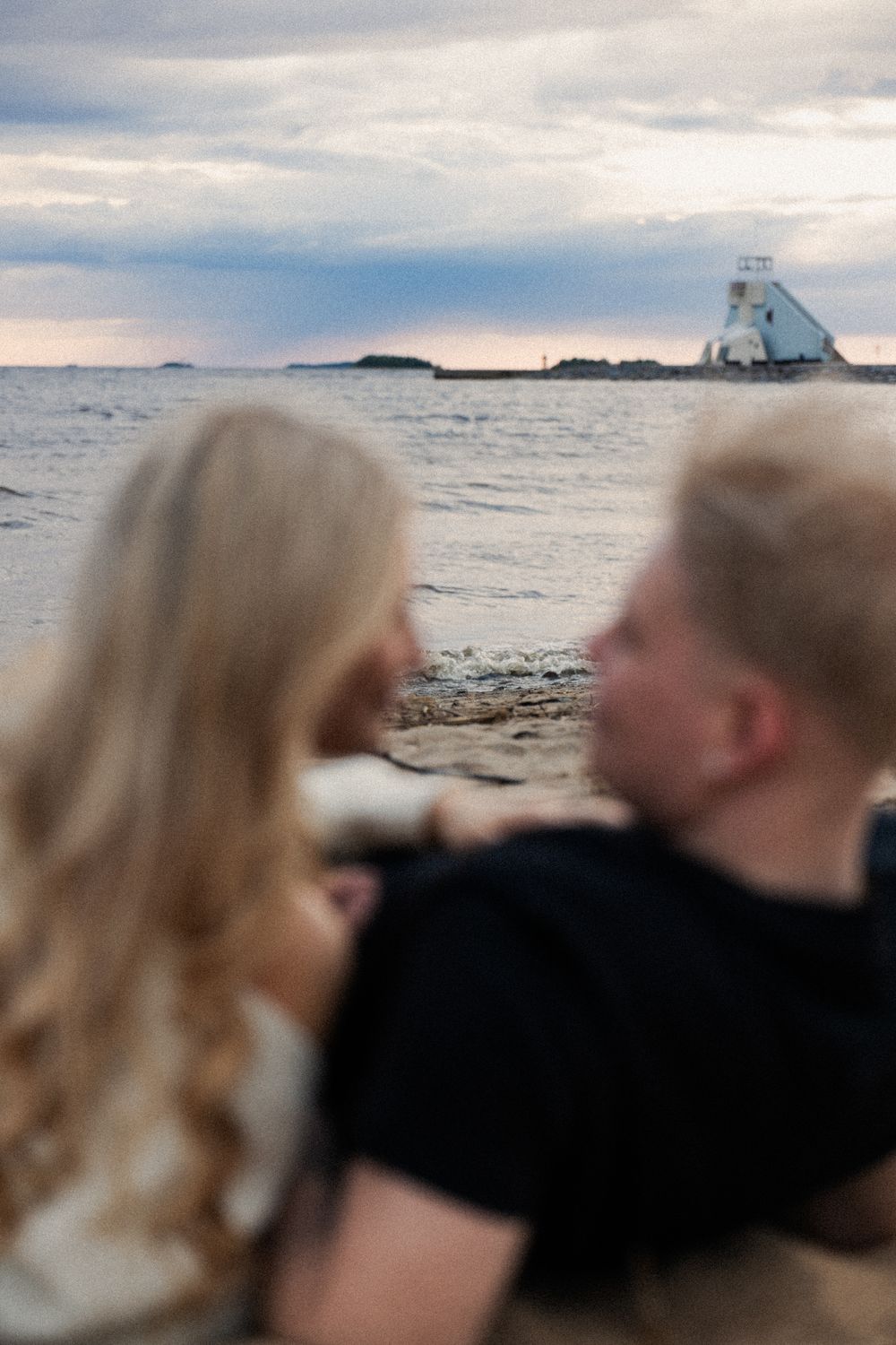 Pariskunta makaa hiekalla majakka horisontissa.