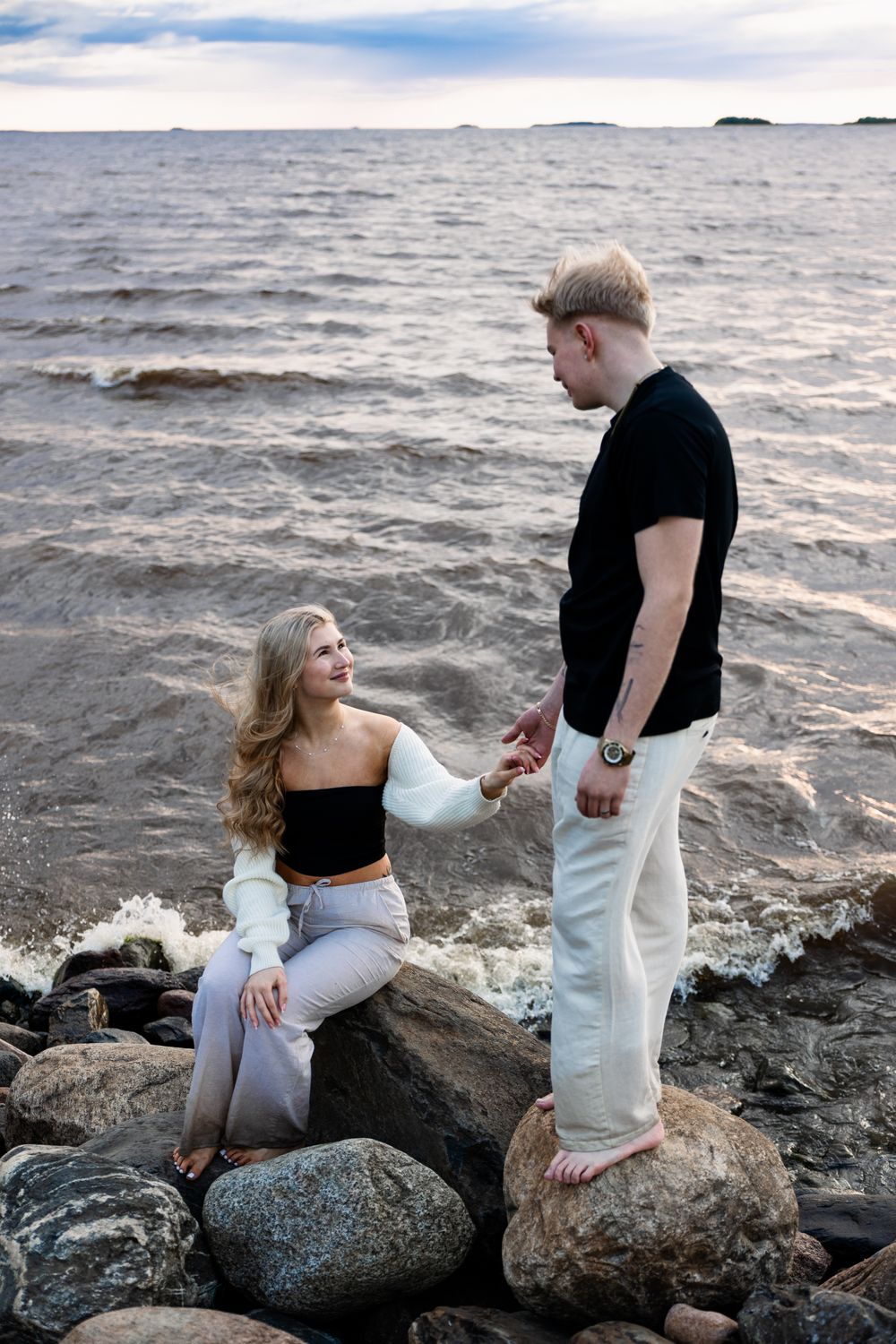 Kihlapari istuu kivillä meren rannassa.