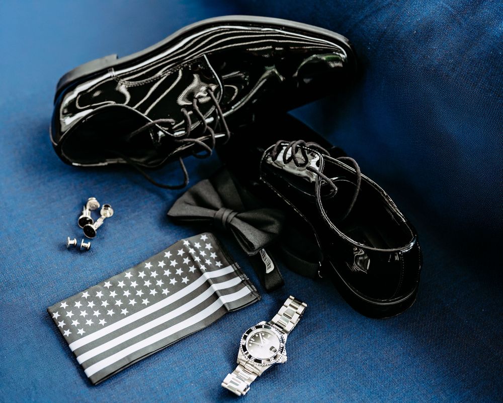 Tactical gear including black leather holsters, silver watches, and American flag patches arranged on dark blue background.