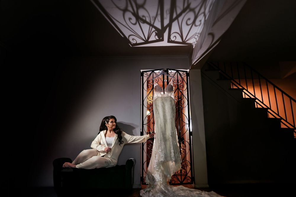 A bride in a white wedding gown stands elegantly in a dimly lit hallway with dramatic lighting and shadows.