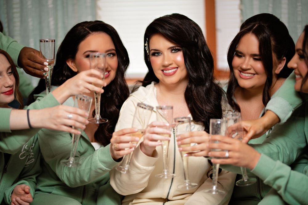 A group of people in green and beige clothing raise their glasses in a celebratory toast at a gathering.