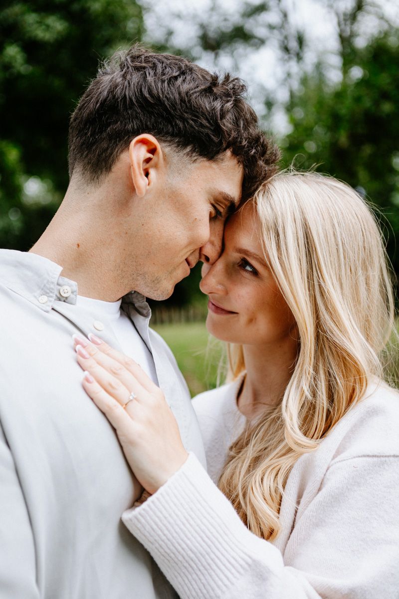 A romantic couple in white sweaters embraces outdoors in a tender moment against a natural background.