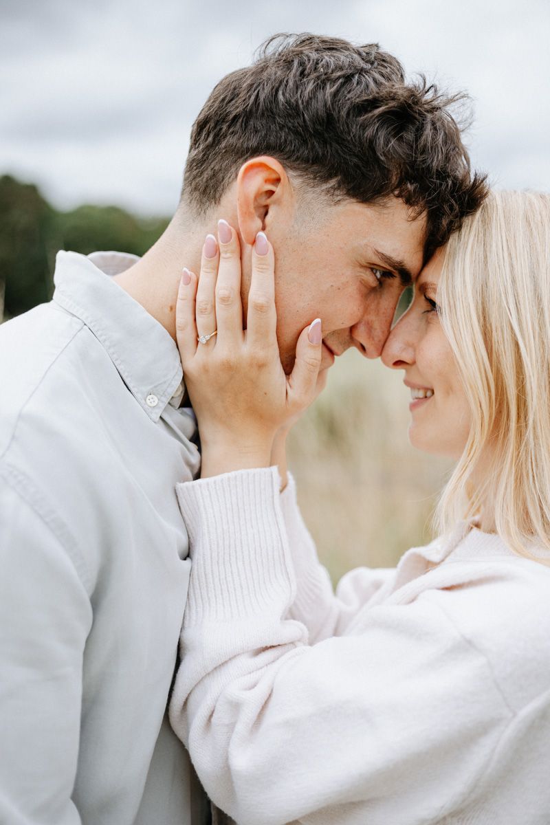 Intimate couple sharing tender moment outdoors, with woman in white sweater touching partner's face.