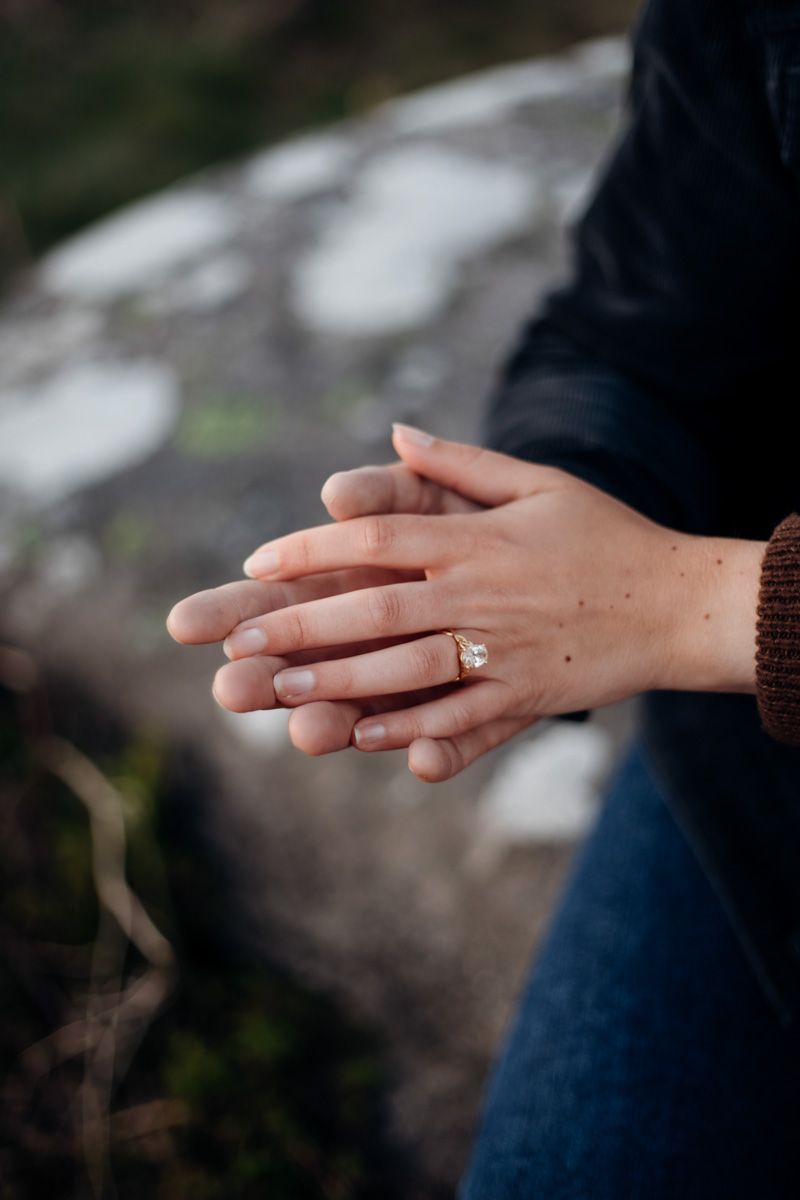 Close-up of woman's hand displaying a large diamond engagement ring, hands intertwined with partner outdoors.