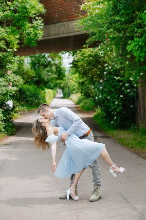 A couple performs a romantic dance dip pose on a tree-lined path during a summer photoshoot.