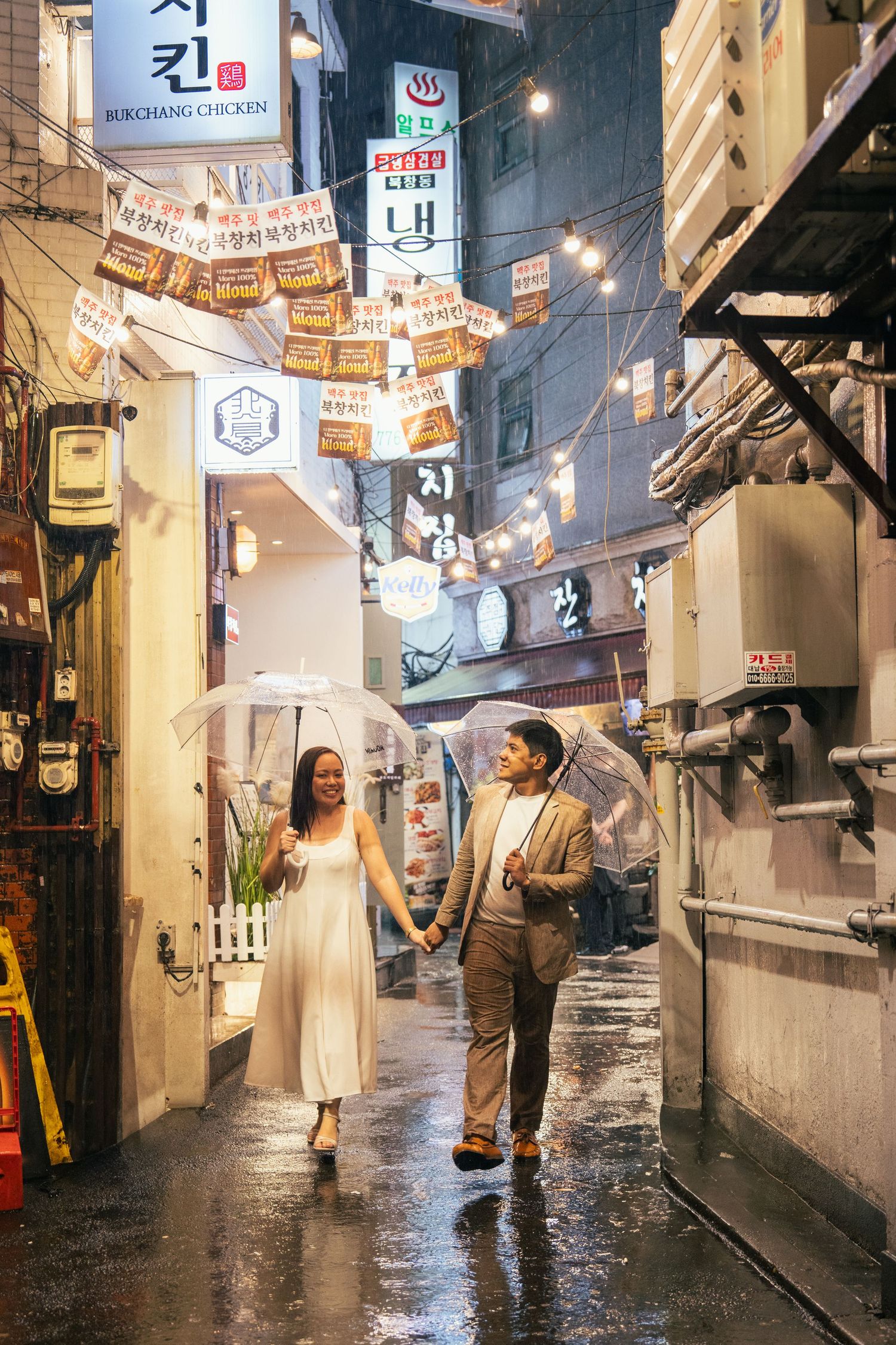 A rainy evening in a narrow alley with glowing lanterns and banners strung overhead in an Asian marketplace.