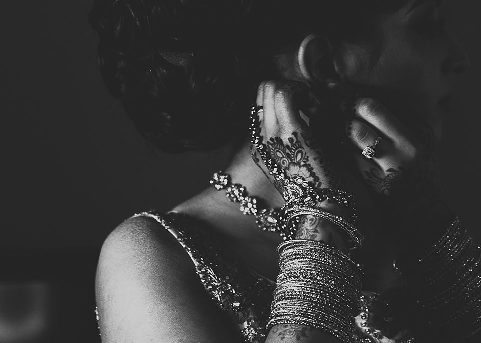 Black and white artistic photograph of a bride's hands adorned with jewelry and henna designs.