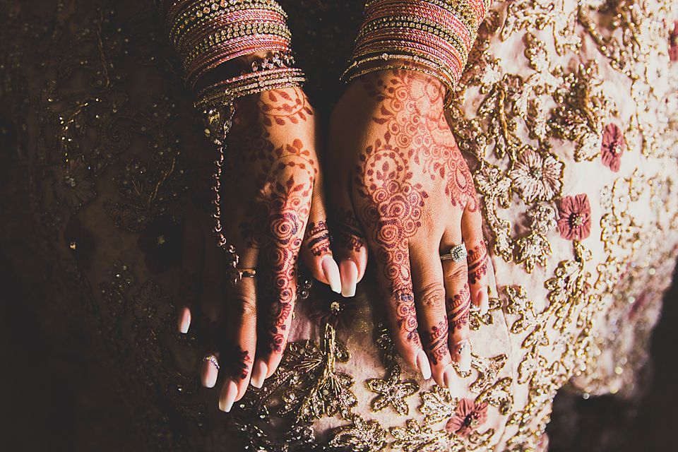 Detailed view of hands decorated with traditional Indian mehndi designs and bridal bangles.