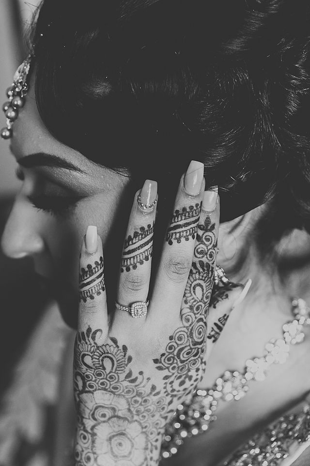 Close up of intricate henna design on hand with neutral manicure and sparkling jewelry details.