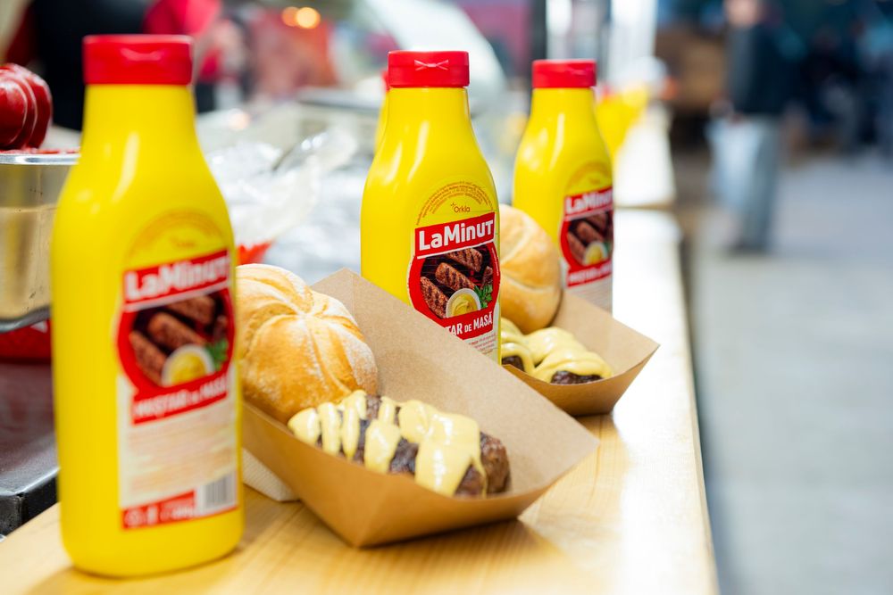 Yellow mustard bottles and food containers arranged in a row on a counter at a food establishment.