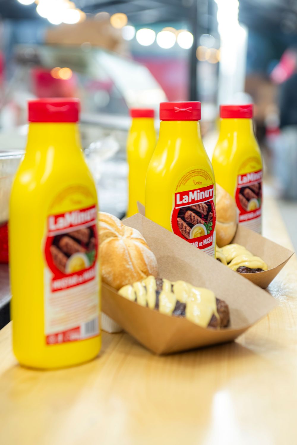 Yellow Leinenkugel's beer bottles and takeout food containers sit on a wooden table with blurred background lighting.