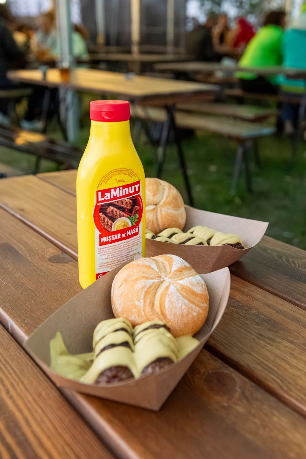 A tangerine and sliced cucumber sandwich served on a wooden table with a yellow bottle of La Minut mustard.