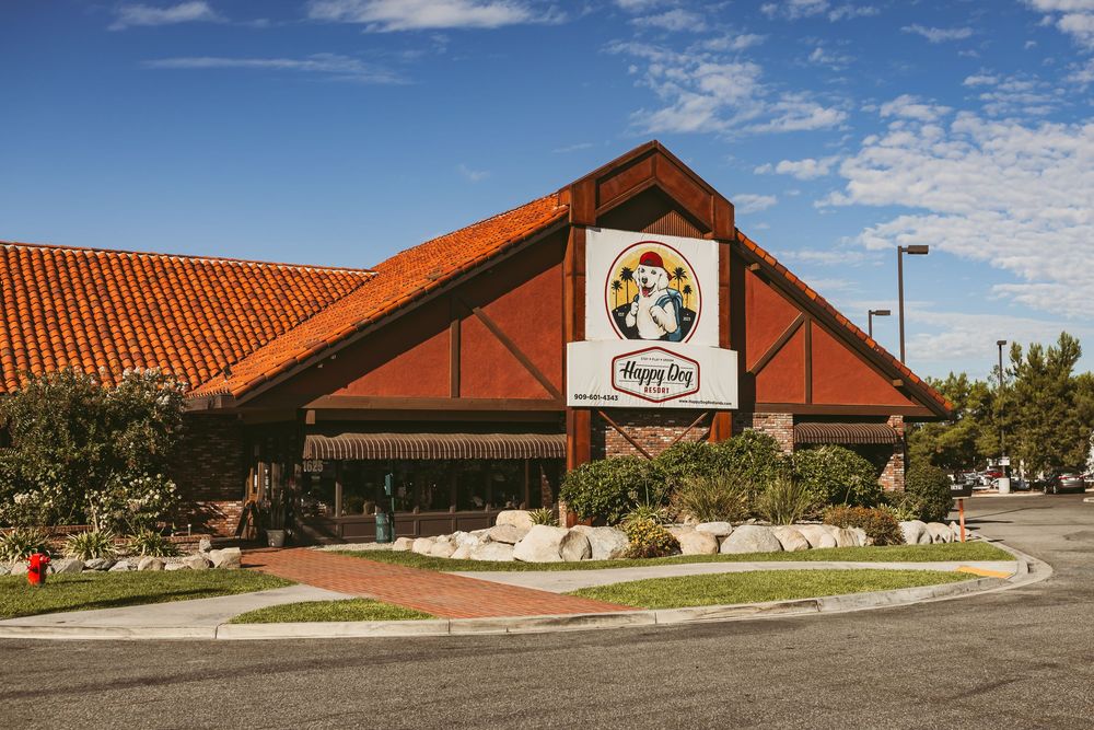 A panoramic exterior view of a modern red-roofed commercial building with multiple connected sections against a blue sky.
