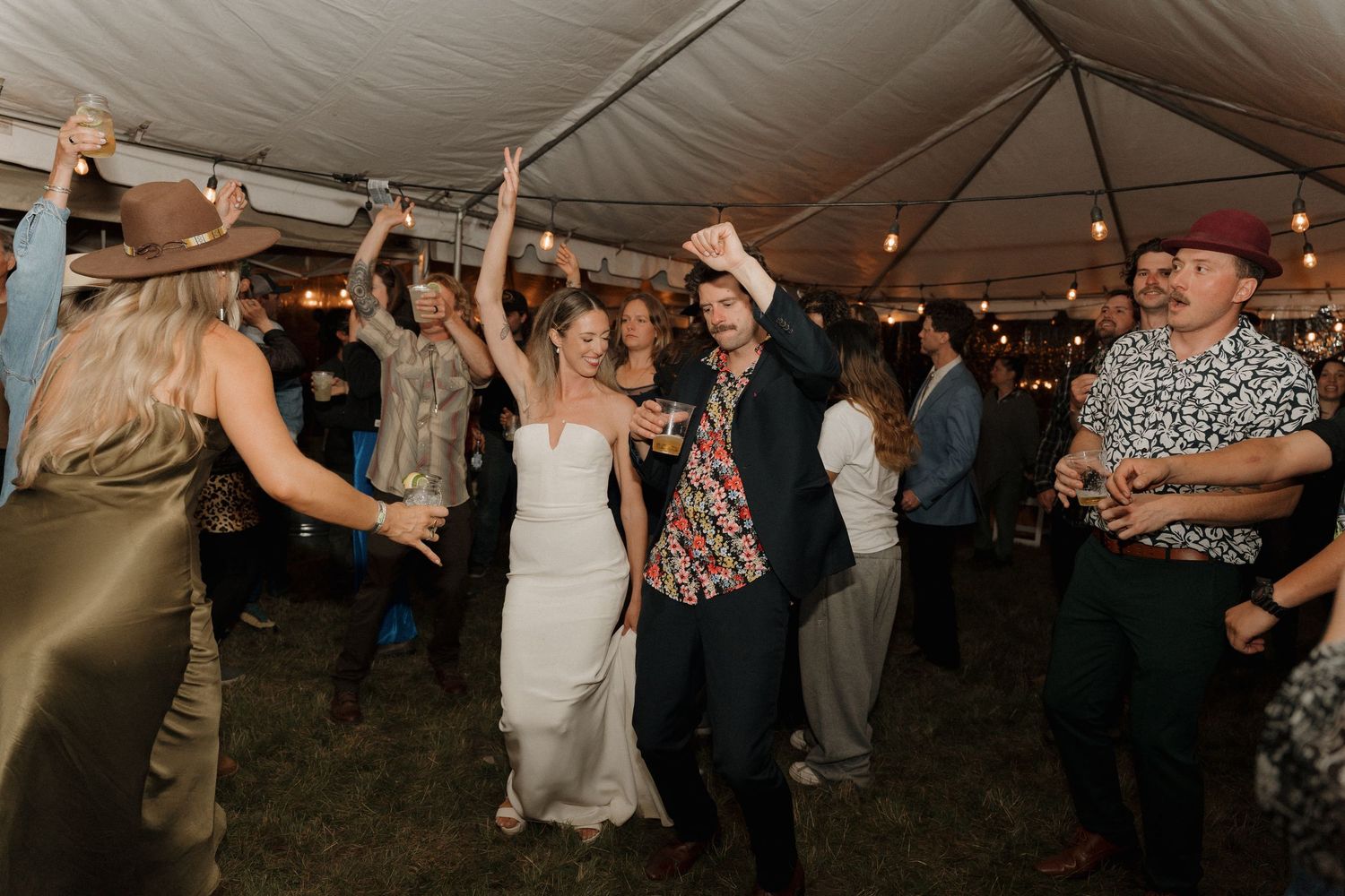 Wedding guests dance and celebrate together under a white tent at an evening reception.