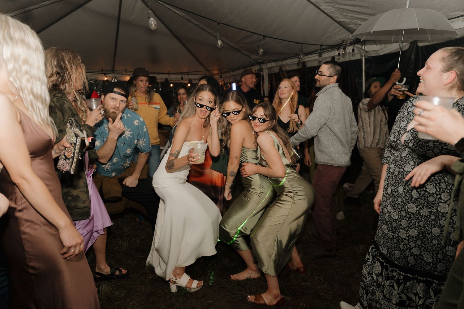 Wedding guests dance and celebrate on a crowded dance floor under a white tent during an evening reception.