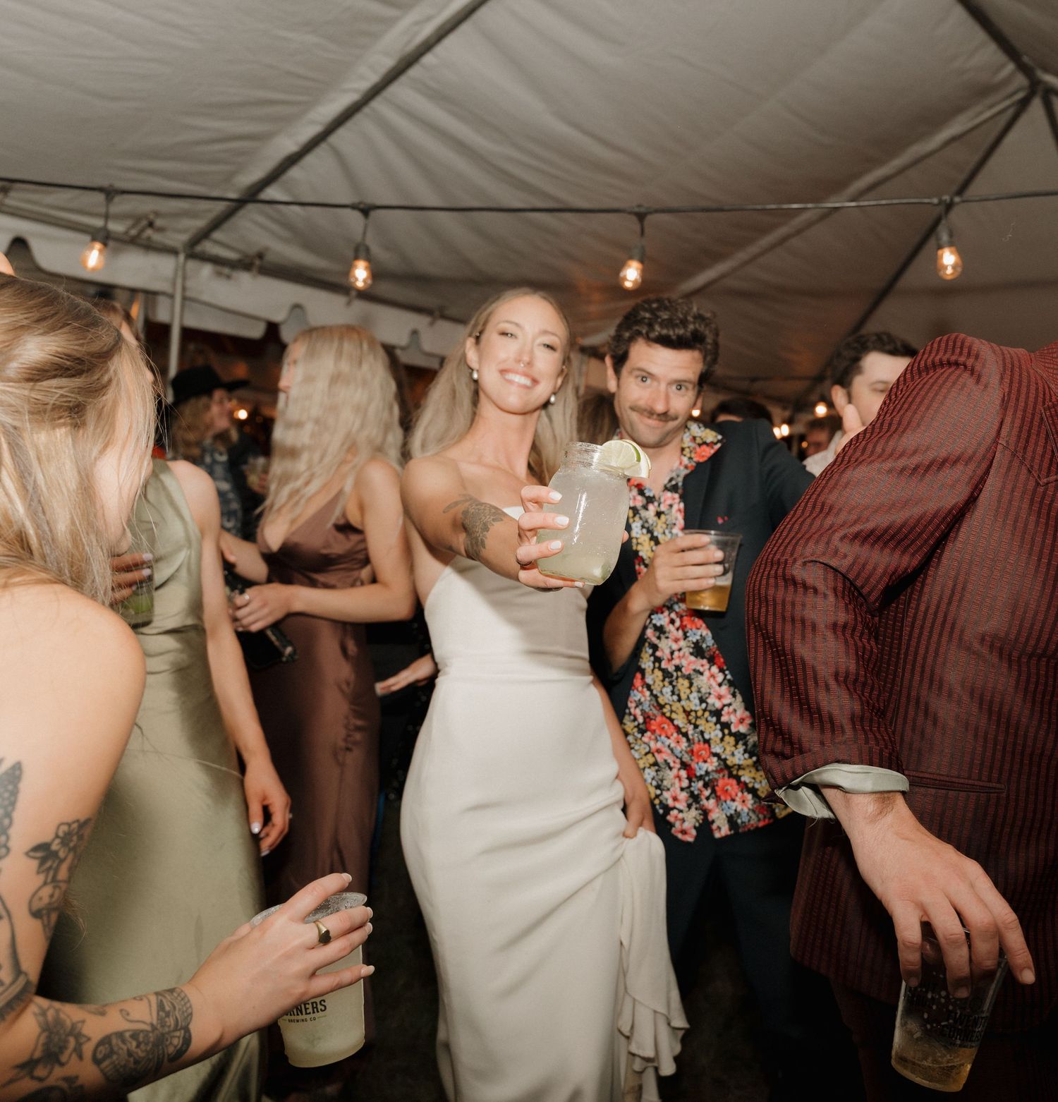 Wedding guests dancing and celebrating on a dance floor under string lights at an evening reception.