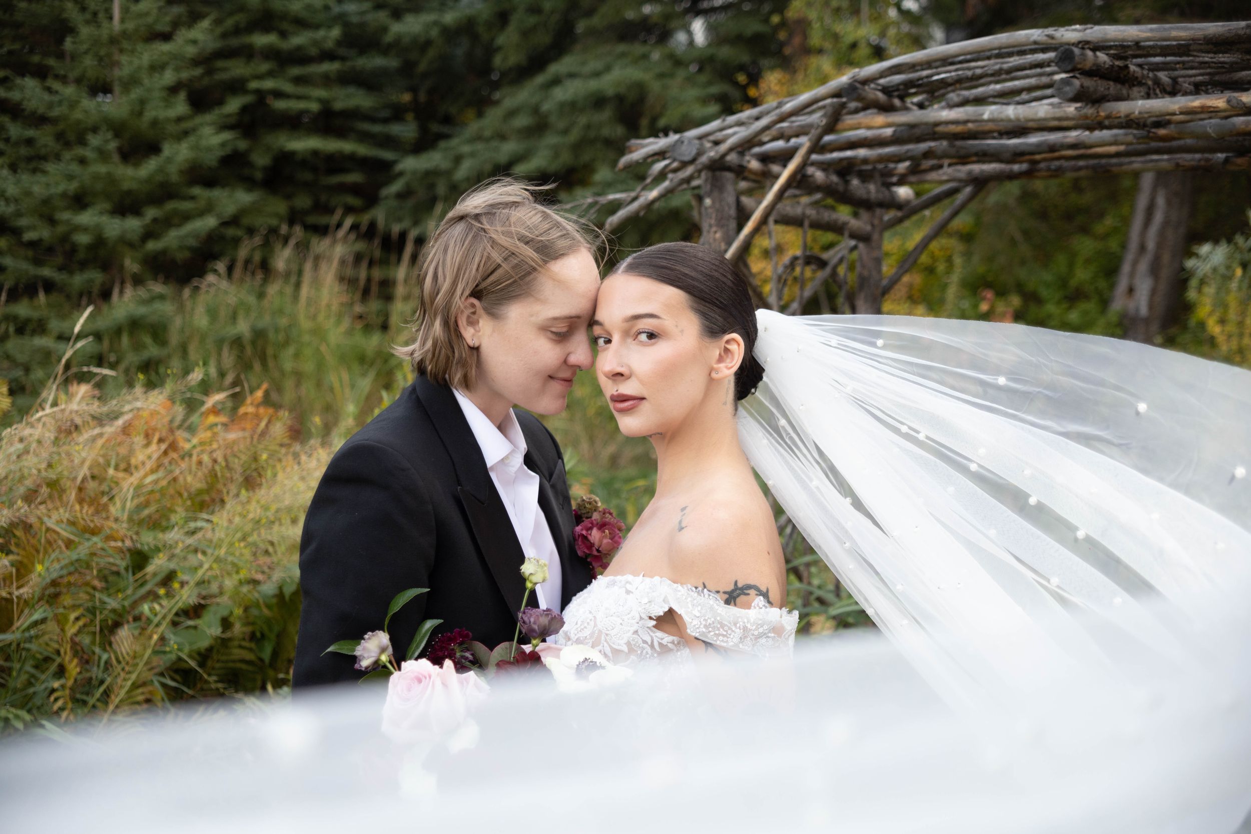 A wedding couple poses together as a veil flows dramatically in the wind.