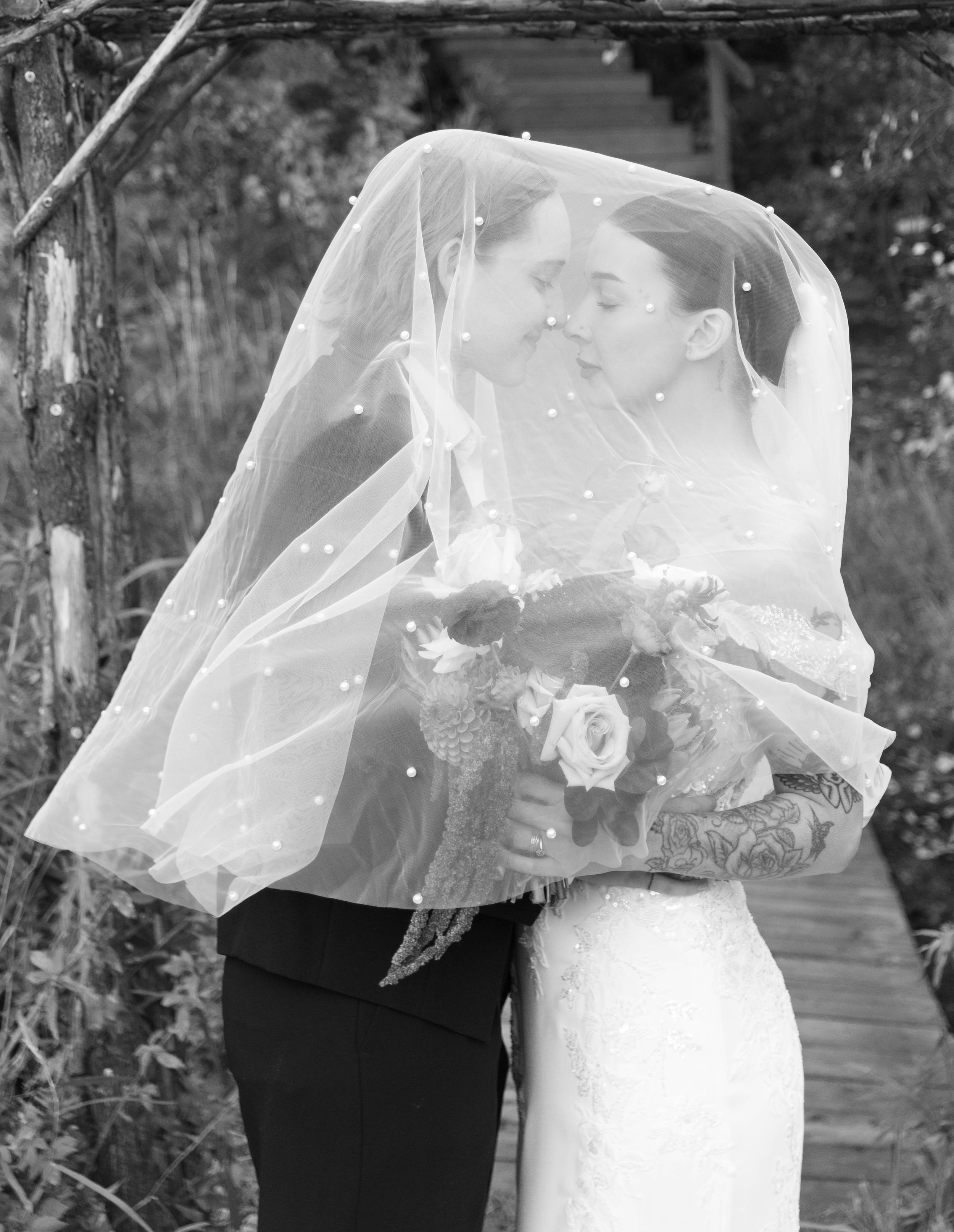 A romantic wedding moment captured through a flowing white veil outdoors.