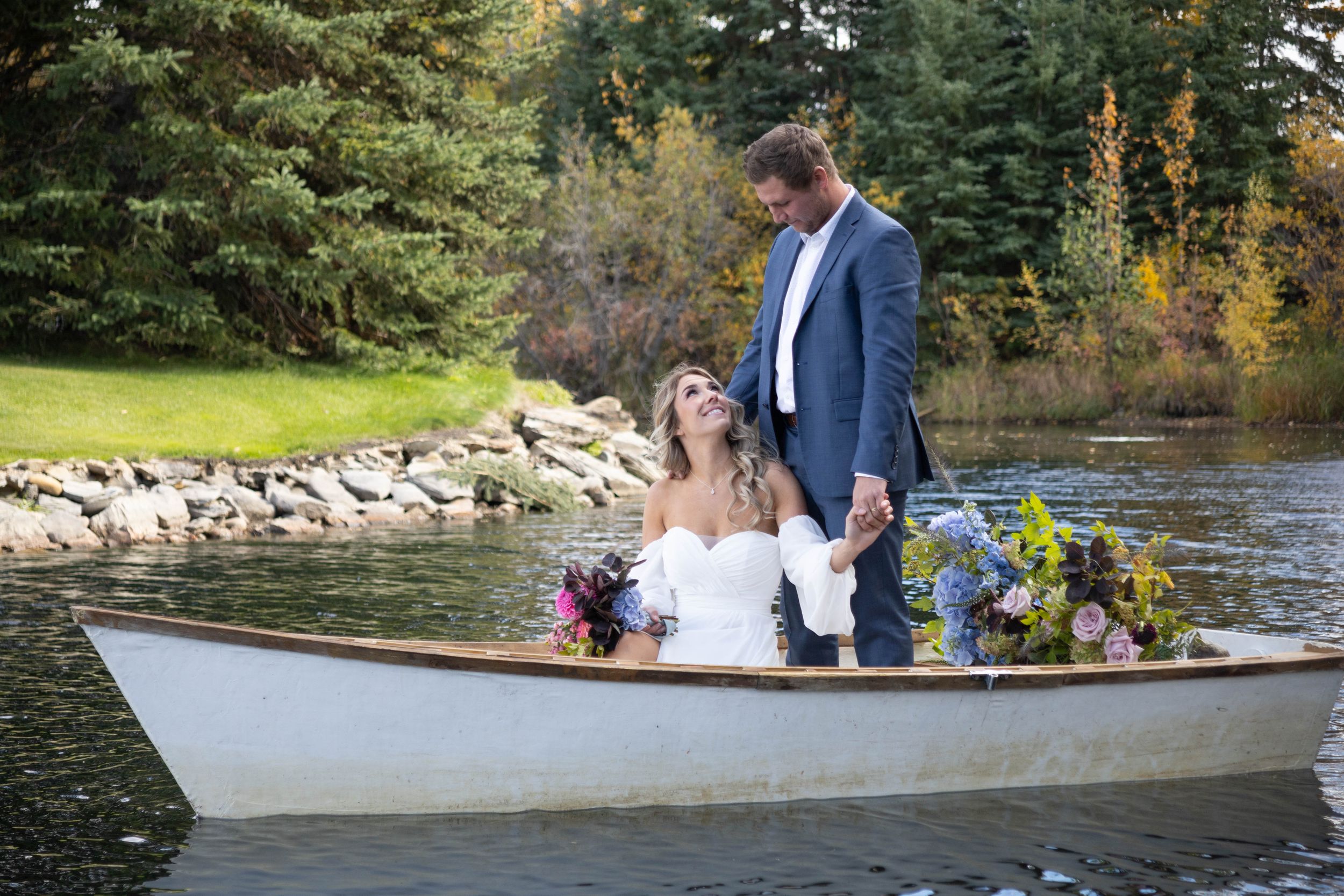 Bride and groom sitting in white boat decorated with flowers on a scenic lake.