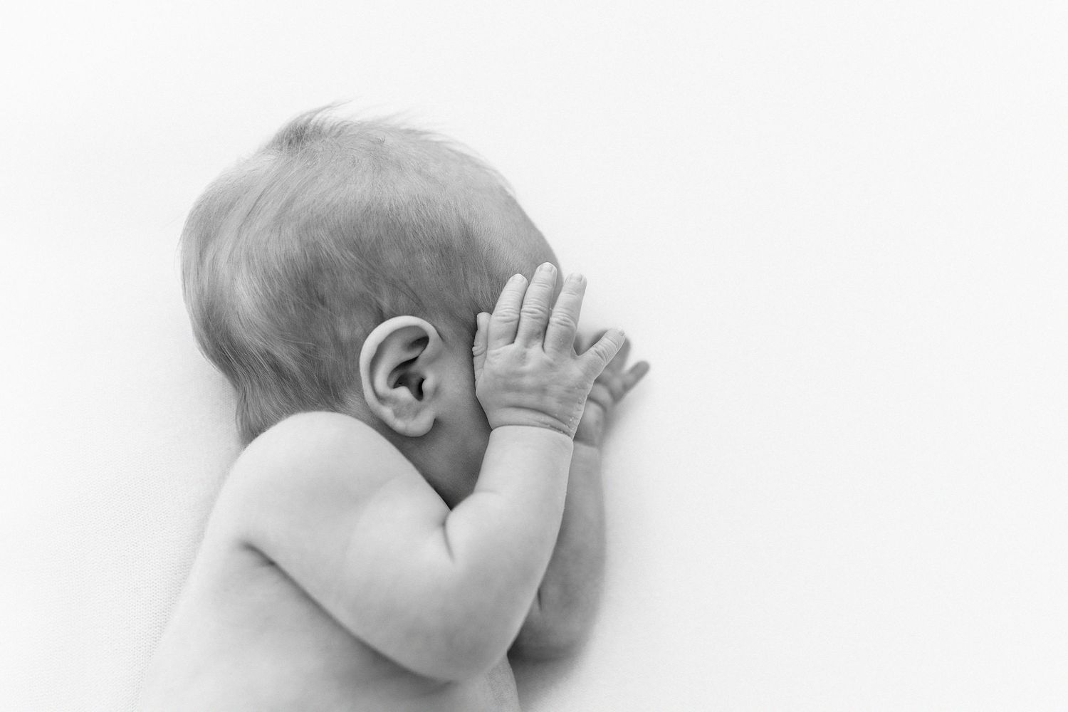Black and white close-up of a baby's head and hand against white background.