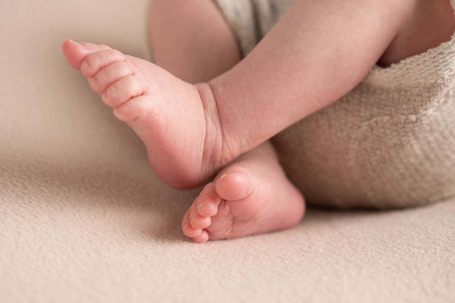Close up of baby's tiny feet resting on beige textile showing delicate skin and toes.