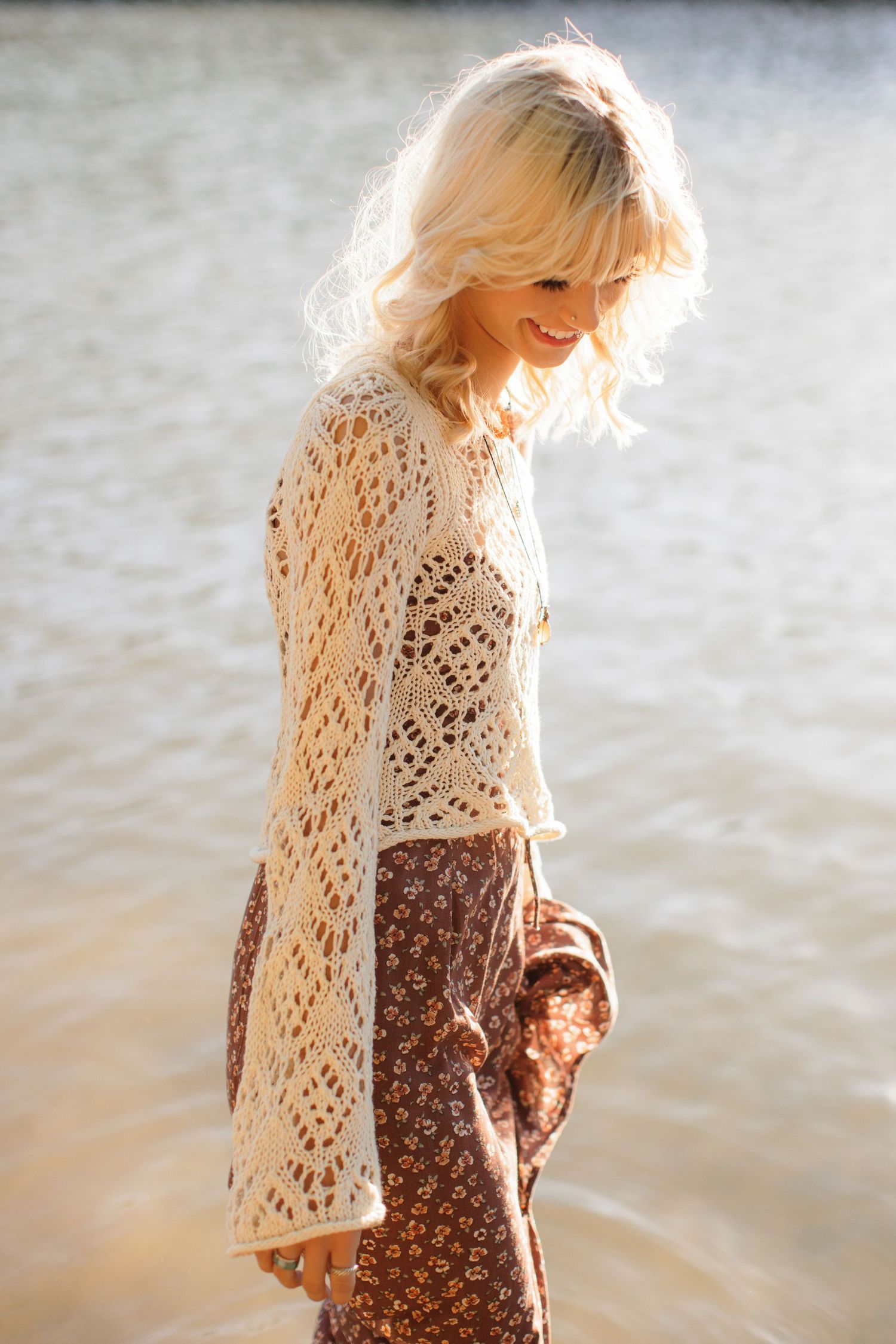 Sun-drenched portrait showing delicate crochet top and flowing skirt by the water.