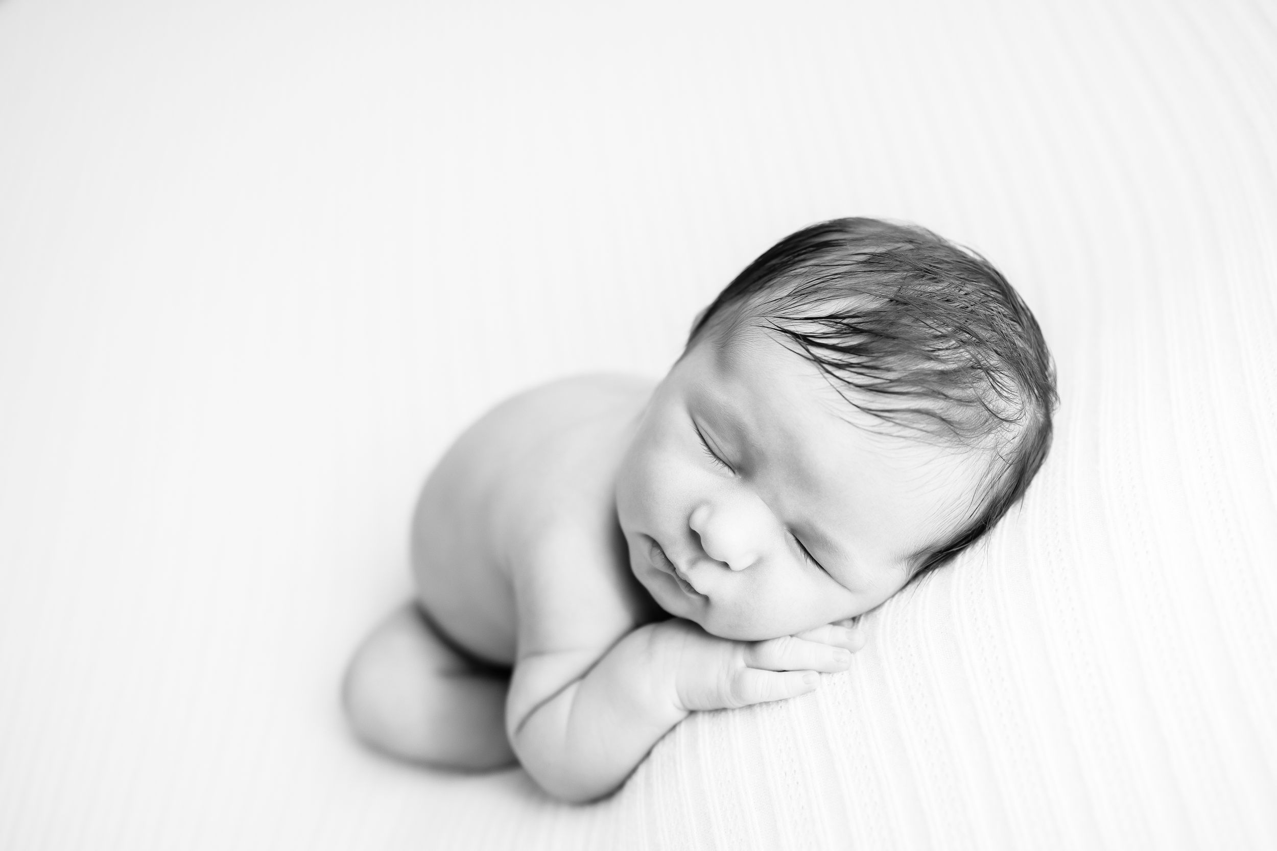 Black and white portrait of sleeping newborn in minimalist setting.